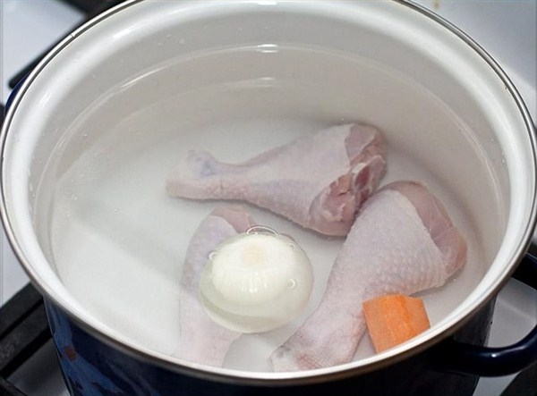В кастрюлю положить помытые куриные ножки, лук и кусочек морковки, посолить и поставить варить